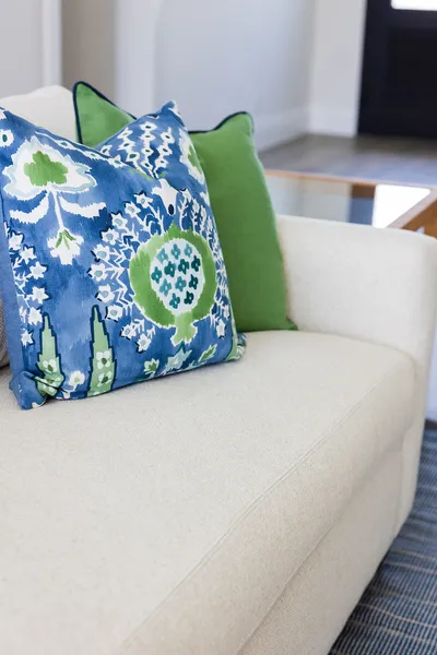 The living room's neutral sofa is adorned with vibrant blue and green throw pillows that reflect the coastal theme, adding a playful and refreshing touch to the decor.
