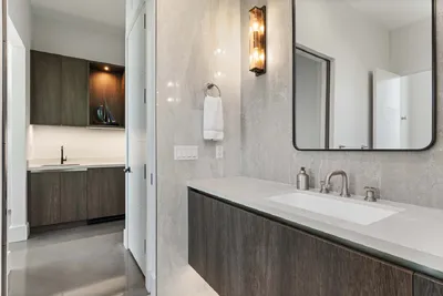 The bathroom features polished surfaces and minimalist fixtures, embodying a clean and sophisticated aesthetic. The warm lighting and streamlined design elements create a calming sanctuary within the modern home.