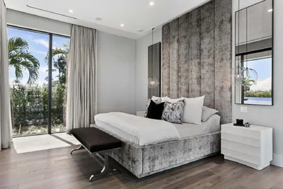 This elegant bedroom exudes comfort and style with its modern decor and rich textures. The large windows flood the room with natural light, offering a soothing view of the surrounding landscape, epitomizing tranquil luxury.