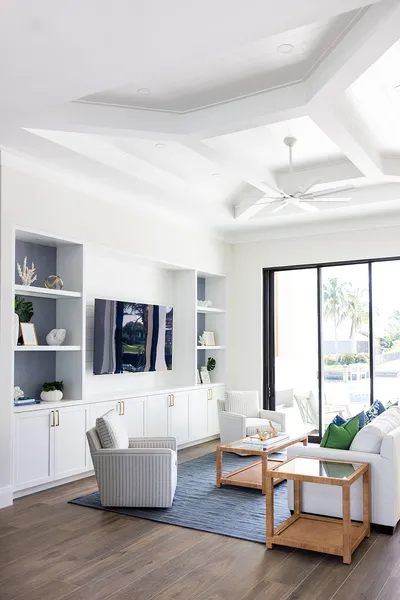 This living room embraces a coastal theme with soft furnishings, nautical decor, and abundant natural light. The seamless indoor-outdoor connection enhances its welcoming atmosphere.